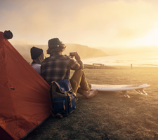 Two people sitting on the beach next to a tent taking pictures of the sunrise.